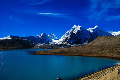 Scenic view of lake and snowcapped mountains against blue sky