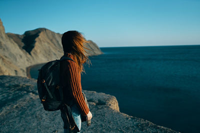 Man standing on rock by sea against clear sky