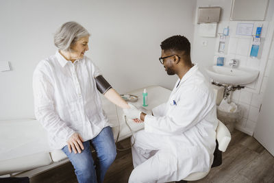 Young male doctor checking blood pressure of female patient at clinic