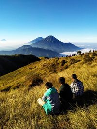 High angle view of male friends sitting on mountain against blue sky