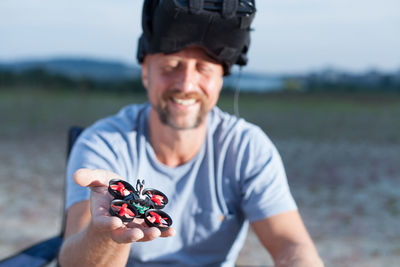 Man holding small drone while sitting on field