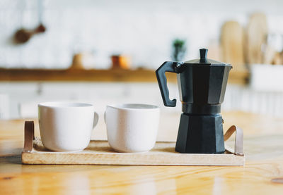 Two white ceramic mugs and geyser coffee maker on wooden tray on the kitchen table