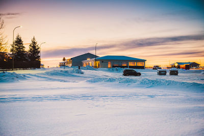 Built structure on snow covered land against sky during sunset