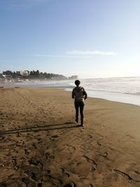 Rear view of man standing on beach against sky