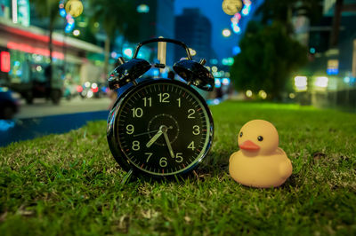 Close-up of clock by toy on grass field at night
