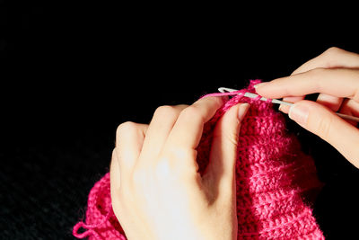 Close-up of woman hand holding pink flower over black background