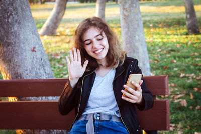 Portrait of young woman standing against tree trunk