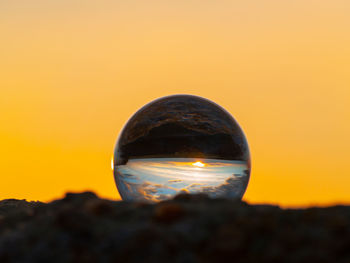 Close-up of crystal ball on rock against sky during sunset