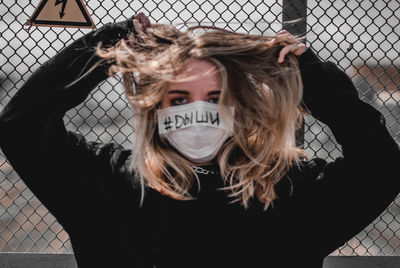 Portrait of woman wearing mask by chainlink fence