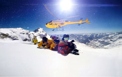 People snowboarding on snowcapped mountain against helicopter flying in sky