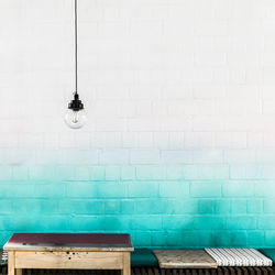 Light bulb hanging against white and turquoise brick wall