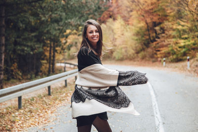 Portrait of young woman standing on road during autumn