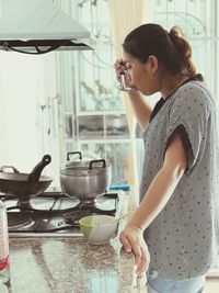 Side view of woman tasting food while standing at kitchen counter