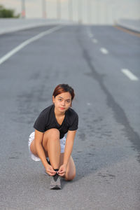 Portrait of young woman tying shoelace on road