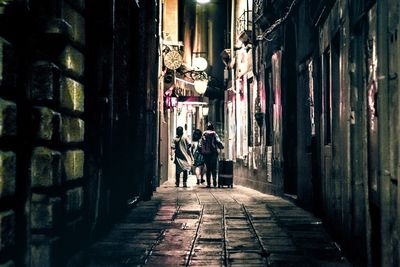 Rear view of people walking on alley amidst buildings in city