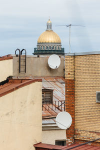 Vertical photo of two white air conditioners mounted on yellow brick wall and two sattelite dishes