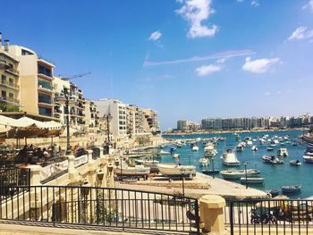 Boats moored at harbor in city against blue sky