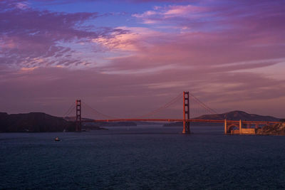 Suspension bridge over sea against cloudy sky