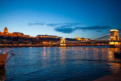 Illuminated city at waterfront against blue sky