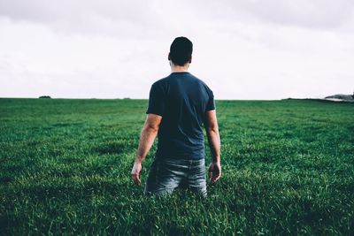 Rear view of man standing in field against sky