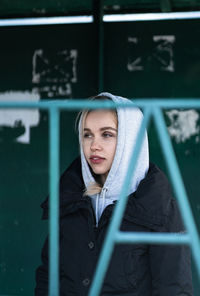 Thoughtful young woman wearing hood standing against wall