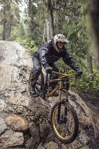 Man mountain biking on fallen tree trunk in woodland