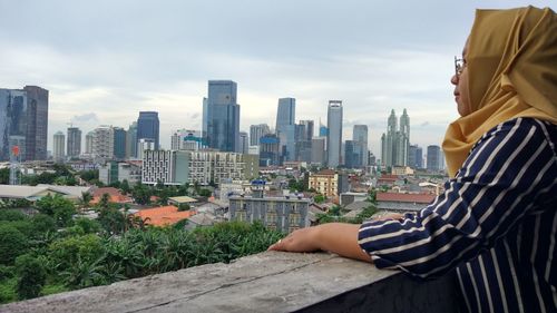 Side view of woman standing at railing against cityscape