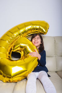 Portrait of smiling young woman sitting against yellow wall