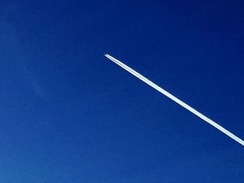 Low angle view of vapor trails against clear blue sky