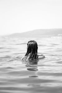 Rear view of woman swimming in sea against clear sky