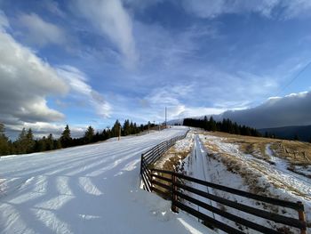 Snow covered road amidst land against sky