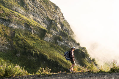 Young woman with backpack hiking in green mountains against clouds summer active lifestyle, outdoor 