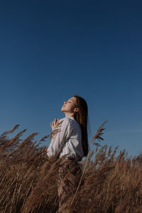 Young woman with closed eyes in white blouse standing in field of dry pampas grass in front of sky