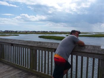 Rear view of man standing by railing against sea