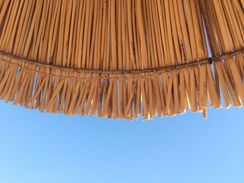 Low angle view of thatched parasol against clear blue sky