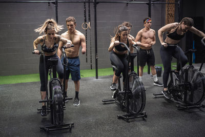 Men motivating women exercising on fitness bike at gym