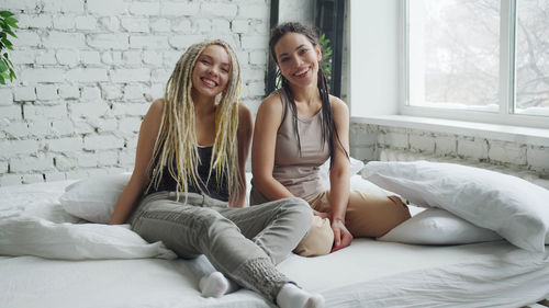 Full length of smiling young woman sitting on bed