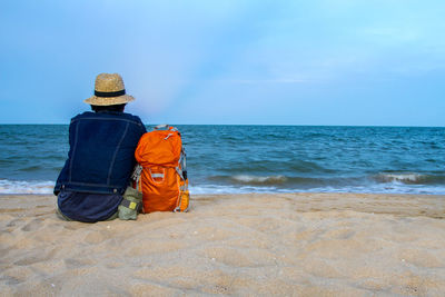 Rear view of man sitting at beach against sky