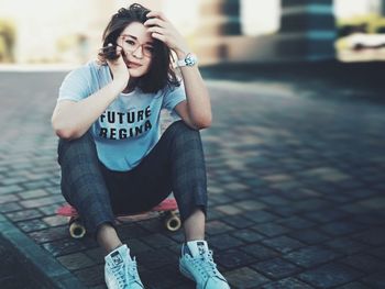 Portrait of beautiful young woman sitting on footpath