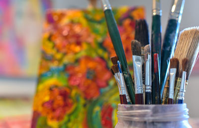 Close-up of paintbrushes in jar with painting in background