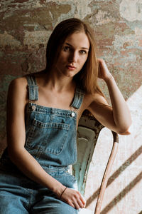 Portrait of young woman sitting on chair against wall