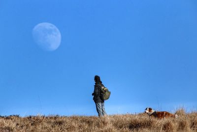 Woman with dog standing on field against sky