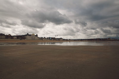 Scenic view of beach by buildings against cloudy sky