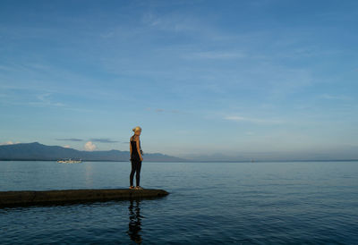 Rear view of woman standing at beach against sky