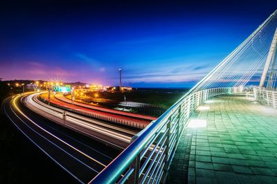 Light trails on street by bridge against sky at dusk