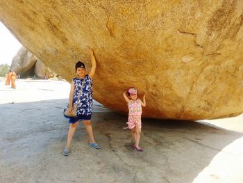 Full length of sisters standing by large rock