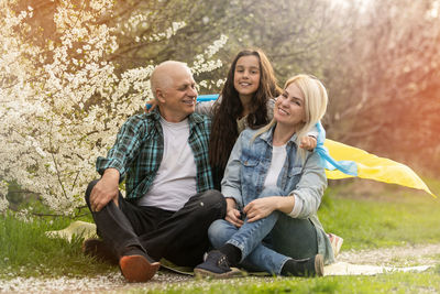 Family with large flag of ukraine in hands against background of a blooming trees. 