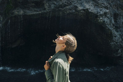 Side view of happy woman standing against rock formation