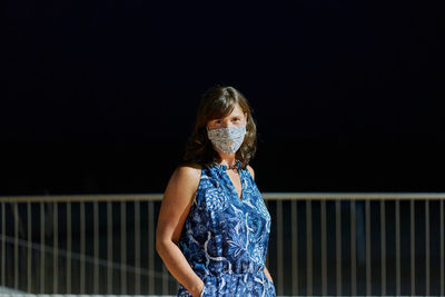 Portrait of woman standing against railing at night