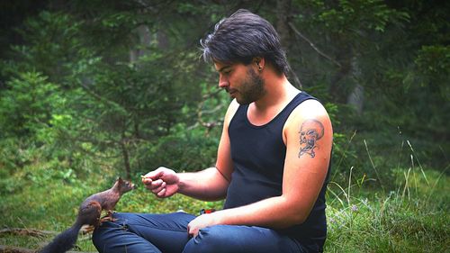 Man feeding squirrel while sitting on field
